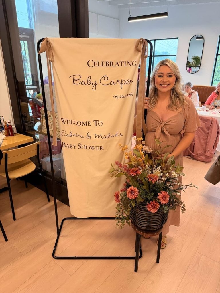 Mom-to-be beside her baby shower welcome sign in the Le Peep Valparaiso private room